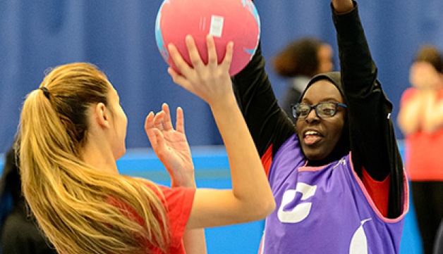 Two schoolchildren playing netball inside a sports hall.