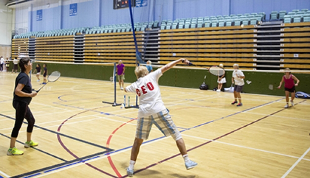 A group of people play badminton in a sports hall.