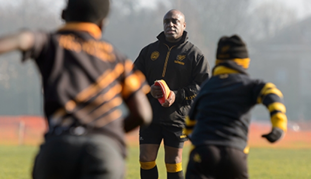 A junior rugby coach watches on as two players run towards him