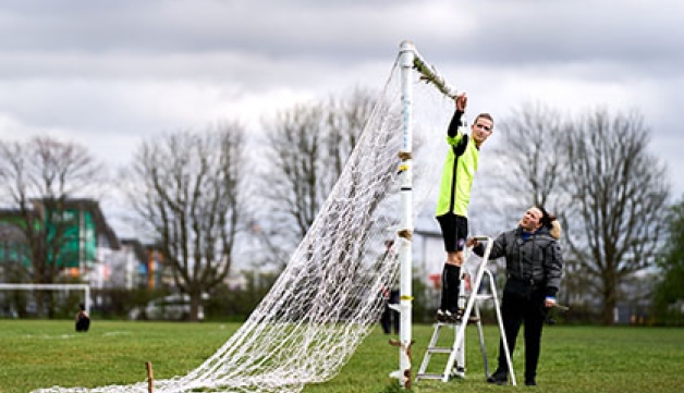 A man and a woman set up the nets on a football goal before a game.