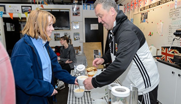 A man serves a woman a cup of tea in a hockey clubhouse