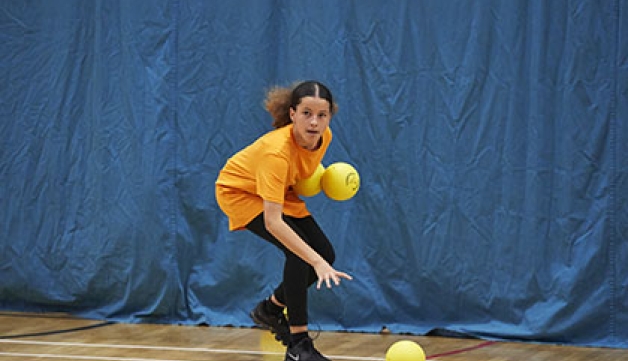 A girls plays dodgeball, holding two balls and trying to pick up a third.