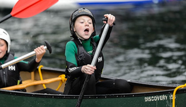 A boy cries out in joy while paddling in a canoe.