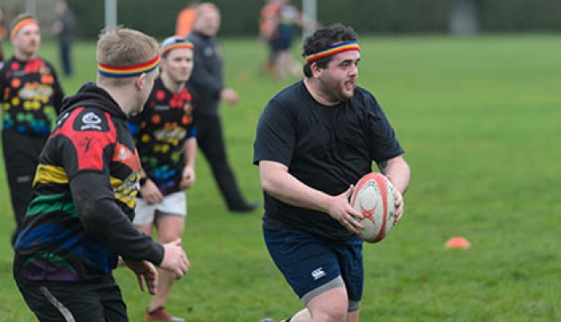A man runs with a rugby ball as two opposition players chase him.