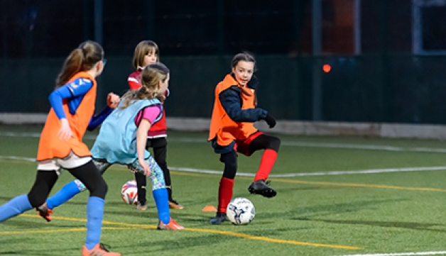 A group of girls play football on an artificial pitch.