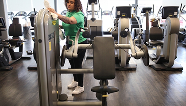 A gym worker wipes down a weights machine