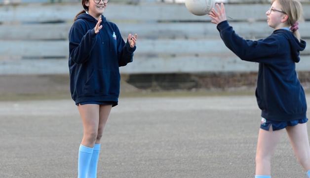 A schoolgirl throws a ball towards another girl during an outdoor game of netball.