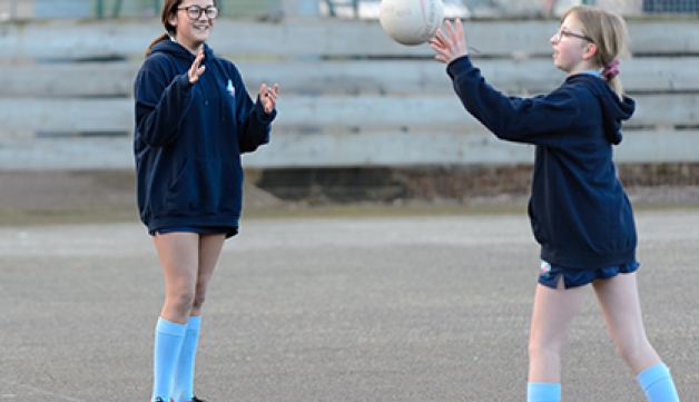 A schoolgirl throws a ball towards another girl during an outdoor game of netball.
