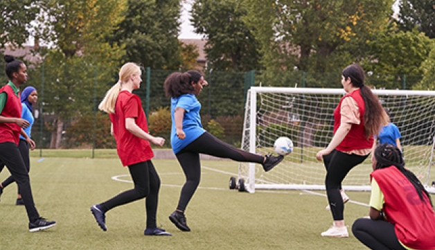 A group of girls play football on an artificial pitch.