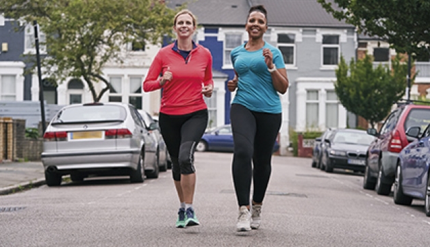 Two women run side-by-side down a road.