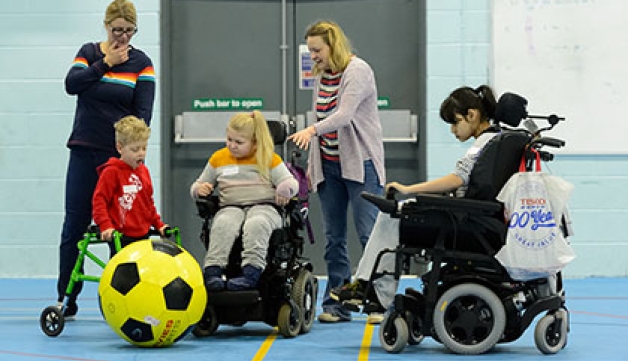 Two child wheelchair users and a and a boy with a walking frame play with a giant football