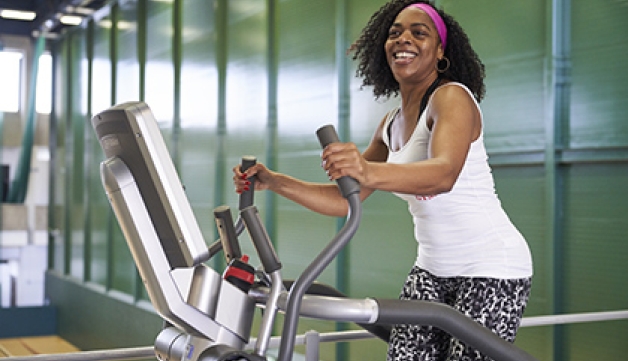 A smiling woman exercises on an elliptical trainer in a gym.