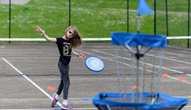 A visually impaired girl throws a frisbee at a target in a playground.