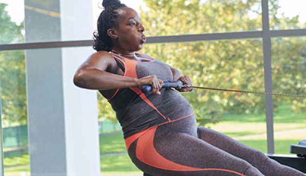 A pregnant women works out on a rowing machine.