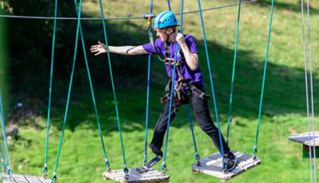 A man with a prosthetic leg walks across a high ropes course.