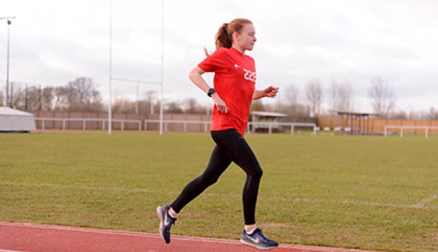 A girl wearing a red TASS t-shirt runs round an athletics track.