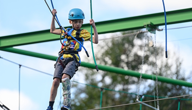 A boy with a prosthetic leg balances on a high ropes course.