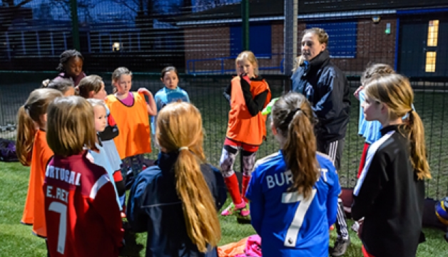 A coach gives instructions to a group of girls at a football coaching session on an artificial pitch