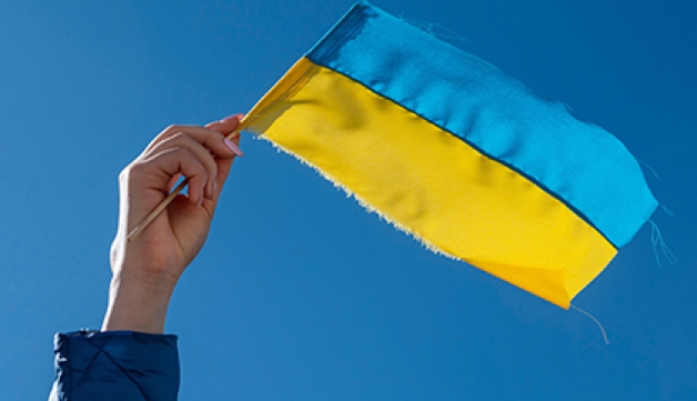A small Ukrainian flag being waved against a blue sky