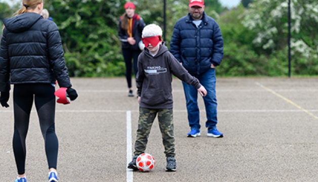 A boy wearing a blindfold tries blind football in a playground