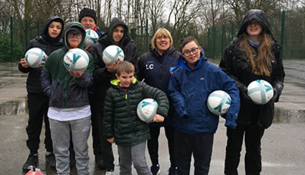 A group of disabled young people, with a coach, stand in a playground holding footballs as they pose for the camera.