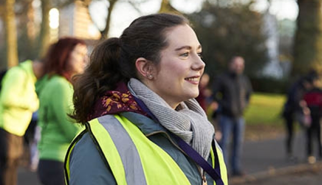 A female volunteer at a parkrun event, with a high-vis vest on and a whistle round her neck