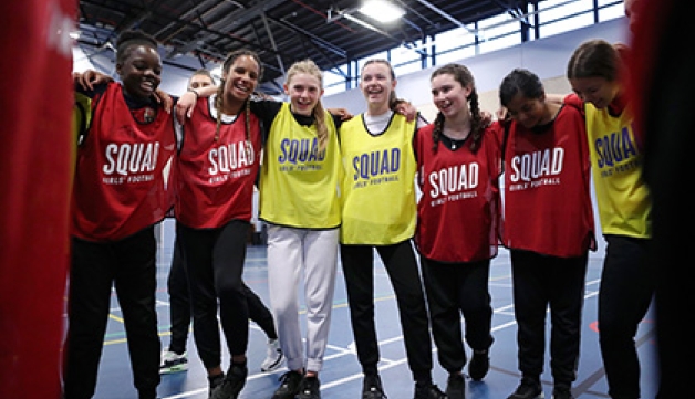 A group of teenage girls gather in a huddle at an indoor football session
