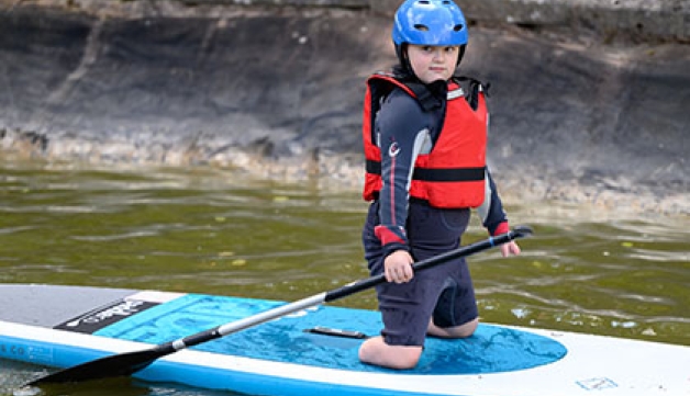 A double amputee-of-the-legs boy, kneels on a paddle board