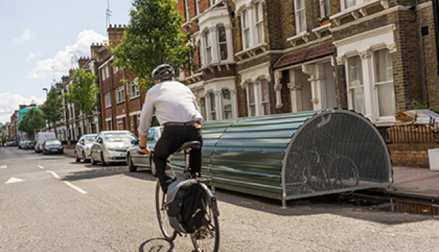Cyclist (motion blurred) passing lockable on-street bike storage