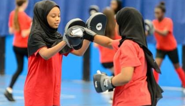 Two girls. wearing dark headscarves and bright red tops, practice their boxing moves in an exercise session