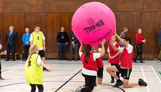 A group of people play with a giant ball on an indoors hall.