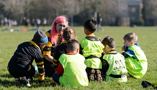 A female rugby coach crouched down with a group of children.