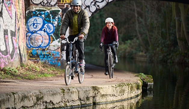 A man and a woman cycle on a canal towpath