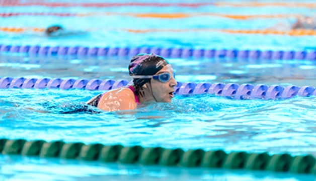 A woman wearing goggles and a swimming hat swims lengths in a pool