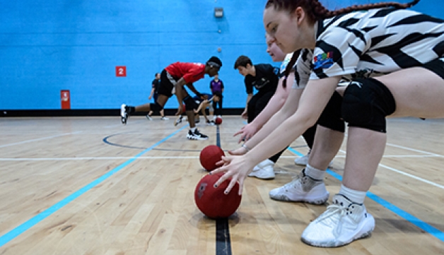 A group of young people reach down to pick up dodgeballs at the start of a game