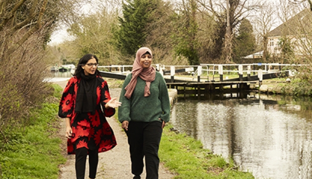 Two women chat as they walk by a canal in the middle of the day.