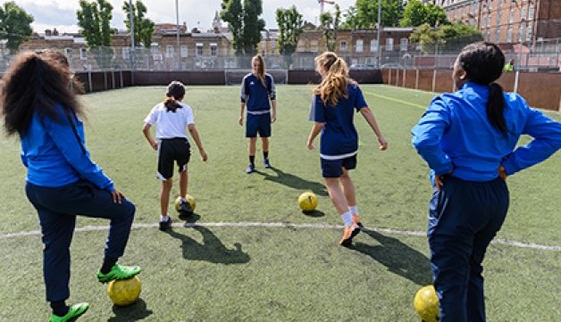 A female coach leads a football training session for girls in a five-a-side pitch