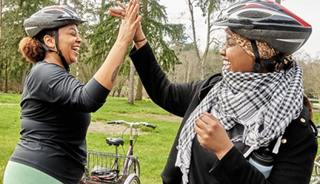 Two women high-five each other next to their bikes on a forest.