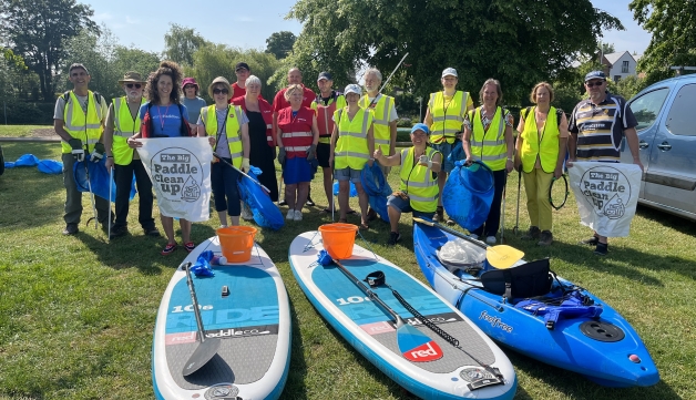 A group of people in high-vis vests pose for a photo, in front of paddle boards and a canoe, holding litter pickers and big bags