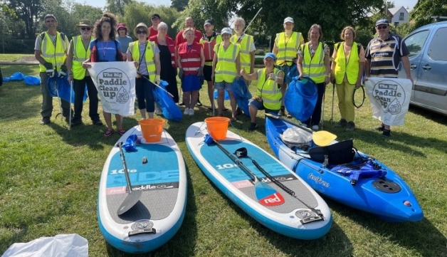 A group of people in high-vis vests pose for a photo, in front of paddle boards and a canoe, holding litter pickers and big bags