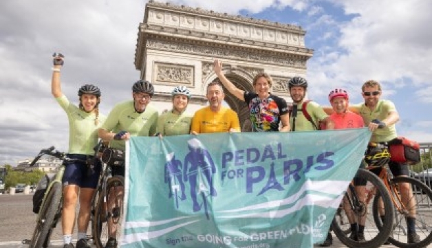 Chris Boardman, Dame Katherine Grainger and the Pedal for Paris cycle team pose with their bikes, a flag and arms raised in front of the Arc de Triomphe.