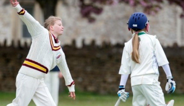 A girl bowls during a junior cricket match as a batter watches on