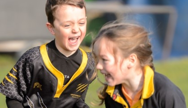 A young boy chases a girl during a game of tag rugby, with both players sporting wide smiles.