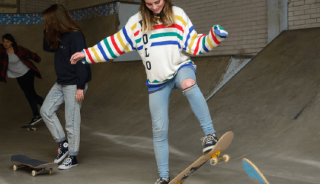 Girl learning to ride skate board in skate park.