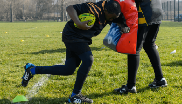 Young boy practicing american football tackle using cushion.