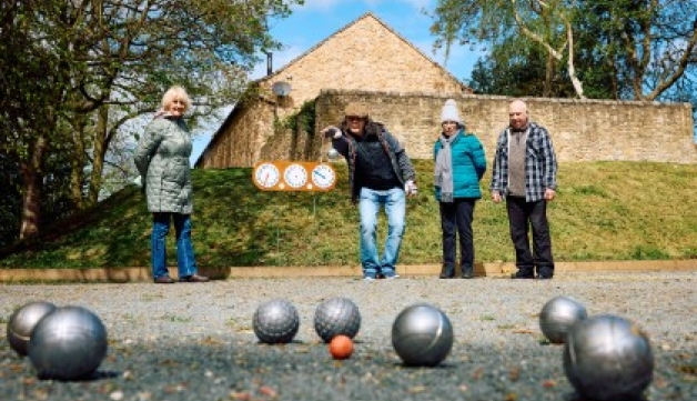 A woman throws a ball during a game of petanque, while three fellow players watch on.