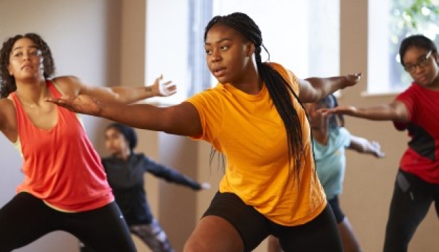 A group of women perform the warrior pose during a yoga class in a studio.
