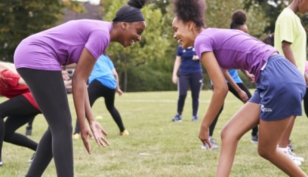 Two girls face other on a field, both leaning forwards in a wrestling stance.