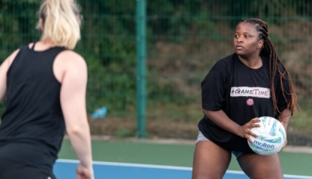 A woman holds a netball on an outside court as an opponent closes in.