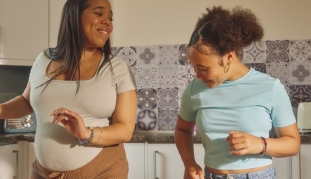 A pregnant woman and a girl dance in a kitchen.